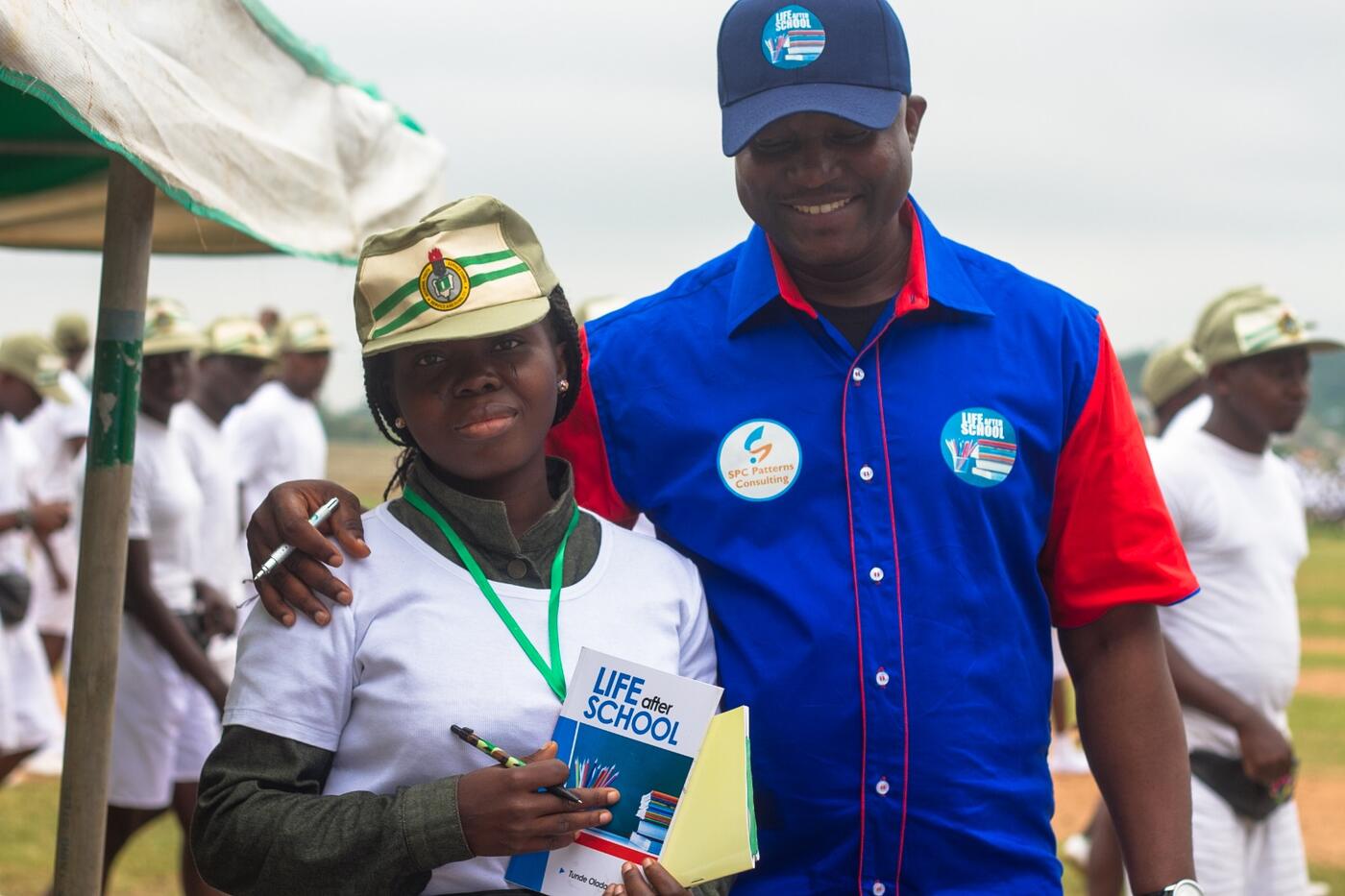 A corps member holding a copy of Life After School beside a facilitator at an NYSC orientation camp